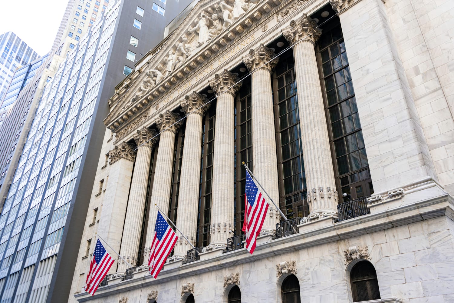 Exterior of the New York Stock Exchange building on Wall Street, with American flags displayed across its facade.